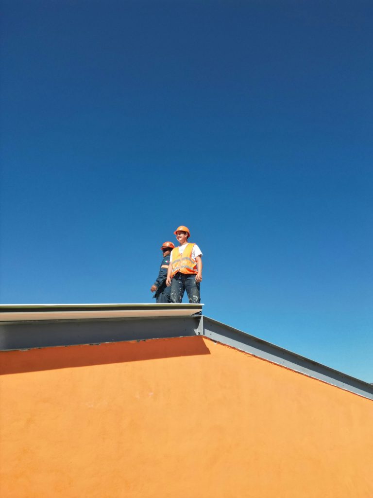 Two construction workers standing on top of a roof.